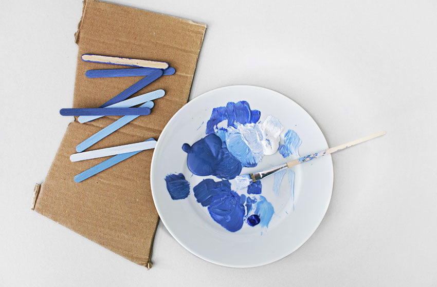 Palette de bleus pour la sélection chromatique sur Repro-Tableaux.com, montrant des bâtonnets de peinture, un pinceau et un mélange de peinture sur une assiette, permettant de rechercher des tableaux par couleur dans leur catalogue étendu.