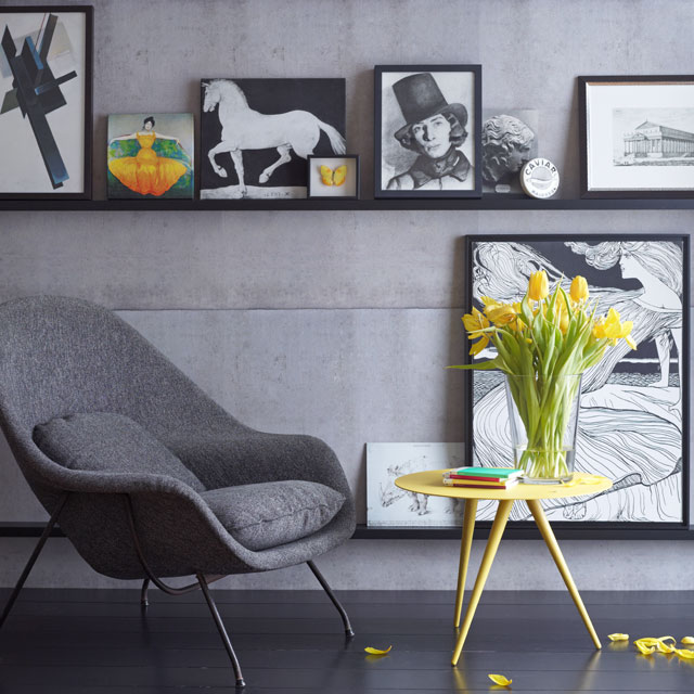 Salon contemporain avec mur galerie affichant un assortiment de peintures artistiques en noir et blanc et en couleur, à côté d'une chaise moderne et d'une table d'appoint jaune vif avec des fleurs jaunes, illustrant l'impact des œuvres d'art grand format 